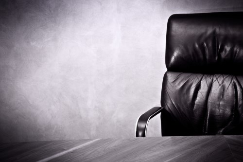 A black leather office chair in front of a concrete wall.