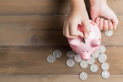 A hand putting coins into a pink piggy bank.