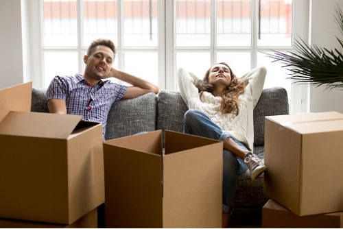 A man and woman sitting on a couch with boxes in front of them.