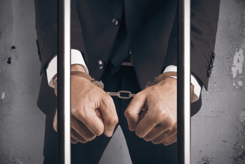 A man in a suit with his hands in handcuffs.