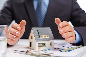 A man in a suit is holding a model of a house.