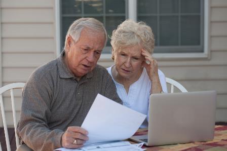 An older couple looking at paperwork on a laptop.