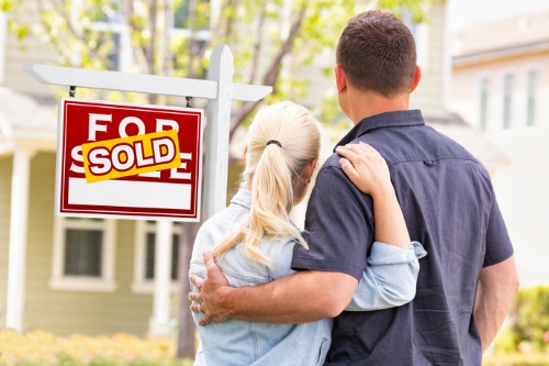 A couple holding a sold sign in front of a house.