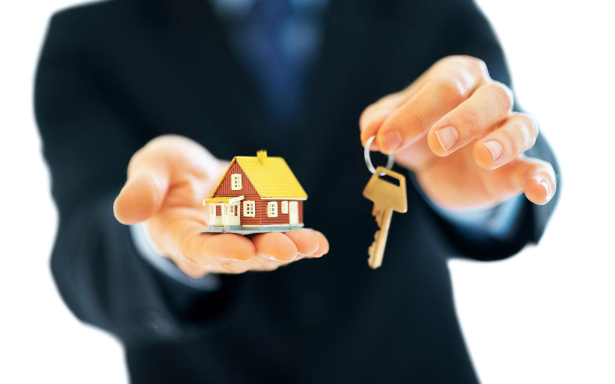 A businessman holding a house model and keys.