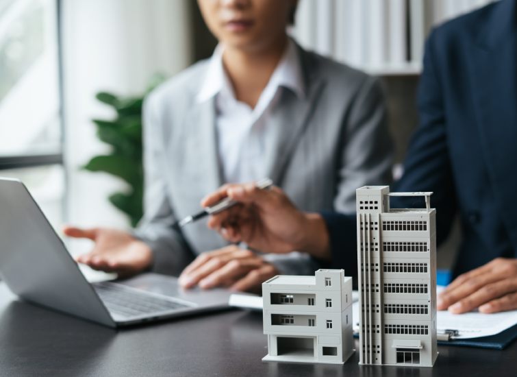 Two asian business people working on a laptop with a model of a building in front of them, engaged in real estate planning.