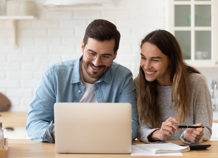 A couple smiling while looking at a laptop discussing mortgage rates.