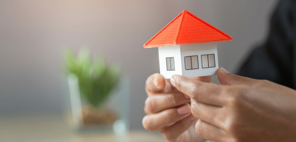 A person holding a rental model house with a red roof.