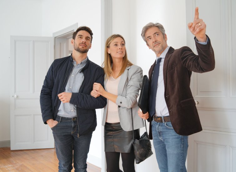 A group of people in the real estate industry standing in a room looking at a new house.
