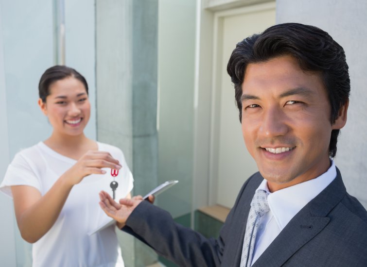 Asian real estate businessman handing a woman a key to her new home.