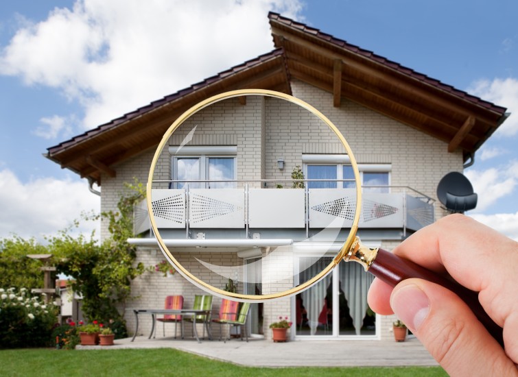 A hand holding a magnifying glass over a house.