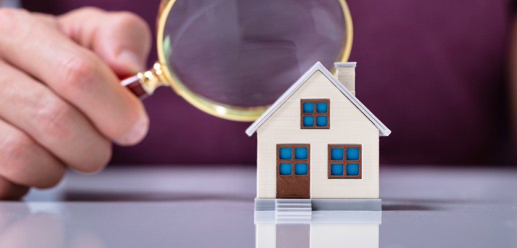 A person is looking at a model house with a magnifying glass.