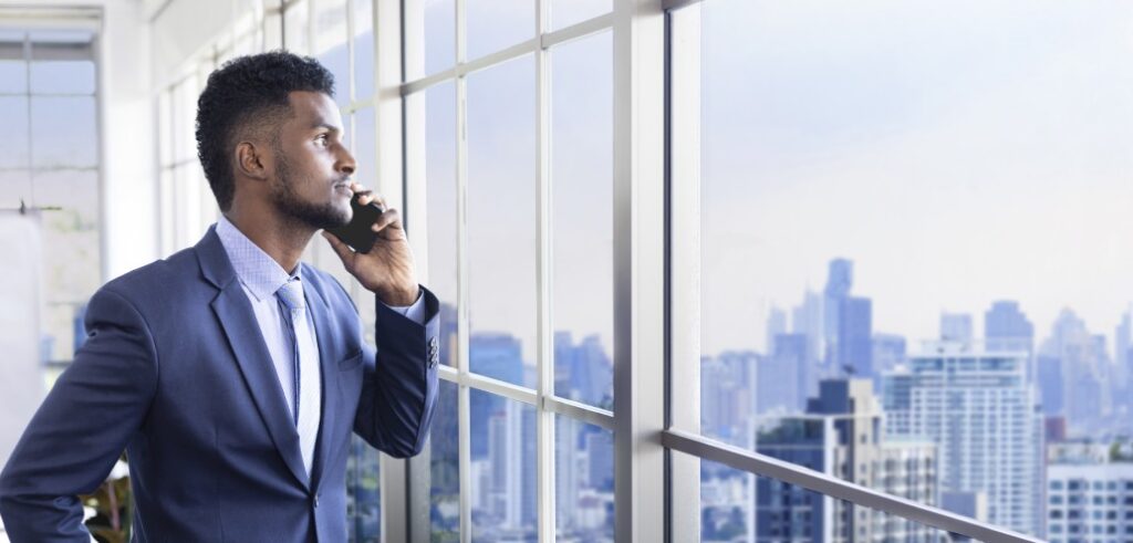 A businessman in a suit is talking on the phone in front of a window.