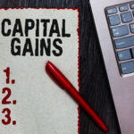 Handwriting text writing Capital Gains. Concept meaning Bonds Shares Stocks Profit Income Tax Investment Funds Piece paper red borders black marker computer keyboard wooden background.