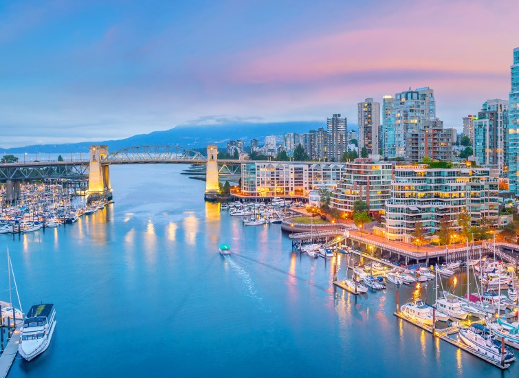 The city of vancouver at dusk with boats docked in the harbor.