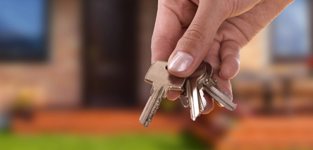A hand holding a bunch of keys with a blurred background of a residential setting.