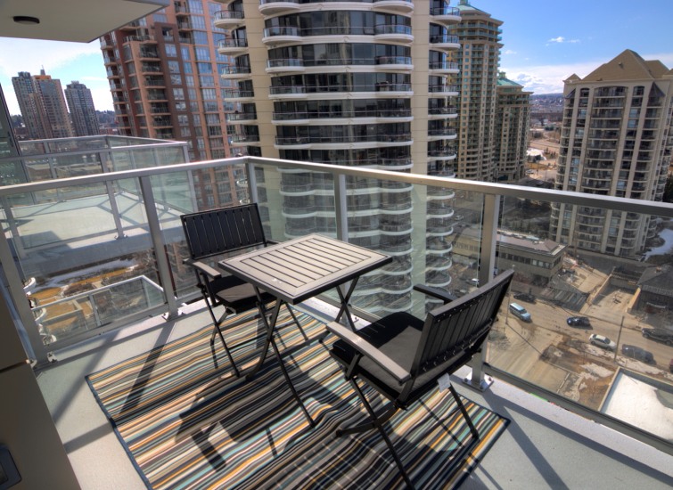 Balcony with a table and chairs overlooking a cityscape on a sunny day.