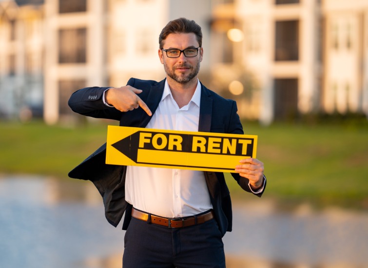A man holding a for rent sign in front of a building.
