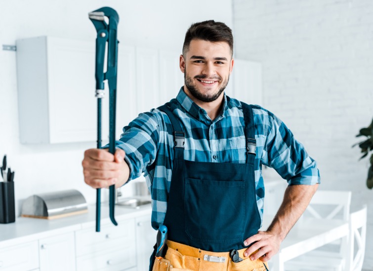 A Canadian plumber holding a wrench in front of a kitchen.
