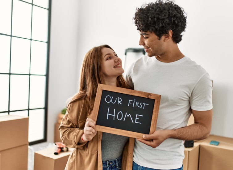 A young couple holding a sign that says our first home.