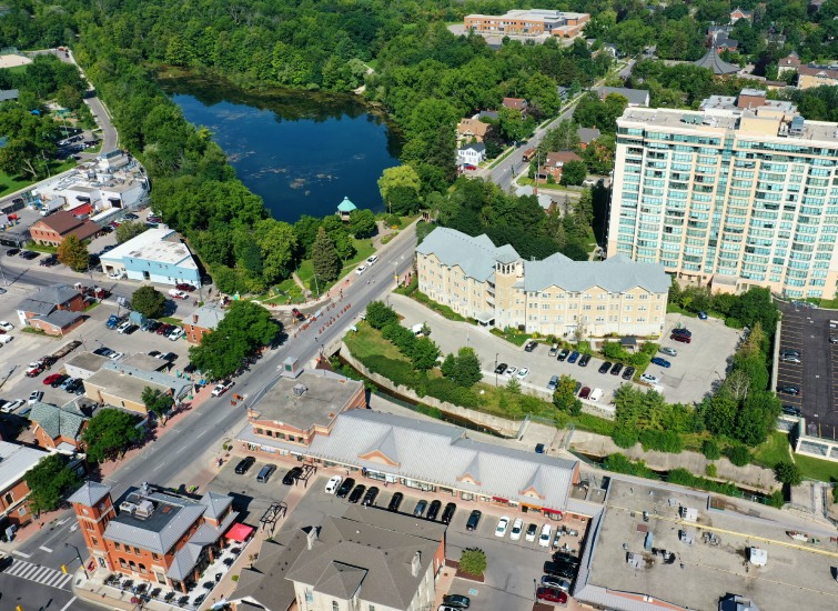 Aerial view of Toronto showing a road, buildings, a lake surrounded by trees, and a high-rise building.