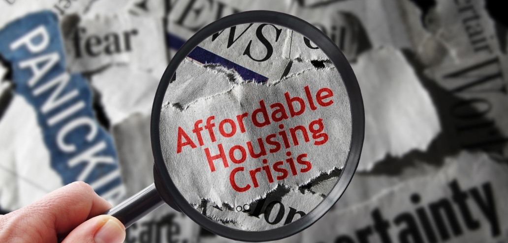A magnifying glass highlighting the phrase "affordable housing crisis" on a background of newspaper clippings featuring words like "fear" and "uncertainty.