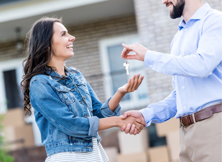 A home buyer handing over house keys to a smiling woman as they shake hands in front of a house during the rescission period.