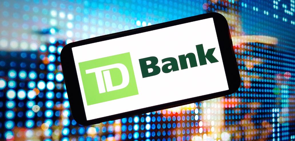 Smartphone displaying the td bank logo, held against a backdrop of a vibrant digital screen with blue pixelated lights.