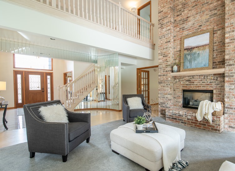 Spacious living room with a high ceiling, brick fireplace, and staircase.