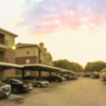 Sunset over a blurred residential apartment complex with parked cars.