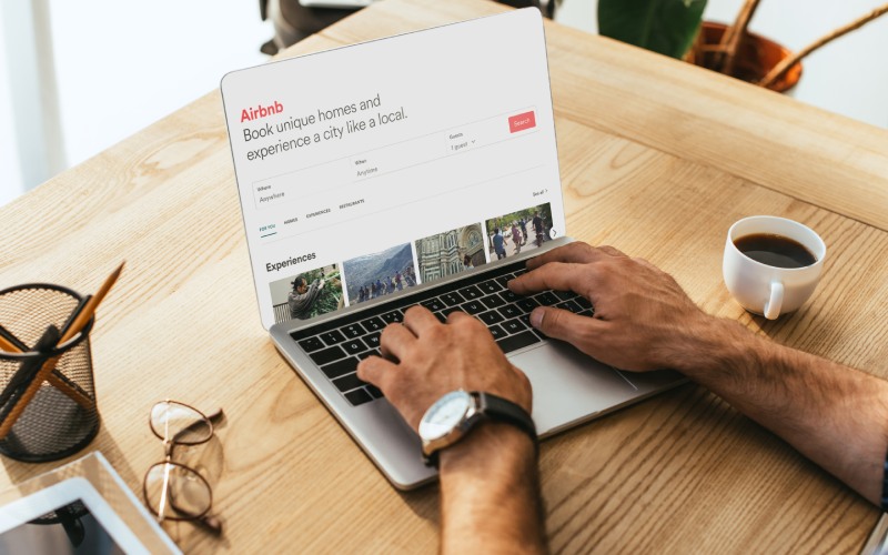 Person browsing Airbnb website on a laptop with a cup of coffee nearby, exploring the latest BC short-term rental changes.