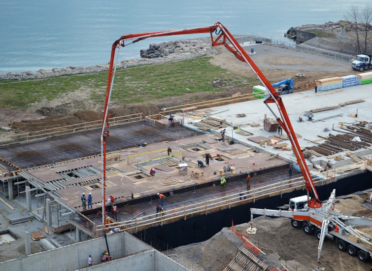 Aerial view of a construction site with workers, featuring a large red crane, near a body of water.