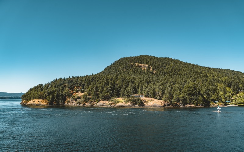 Tree-covered island with a boat passing by in a calm blue waterway, well-suited for BC Short-Term Rental Changes.