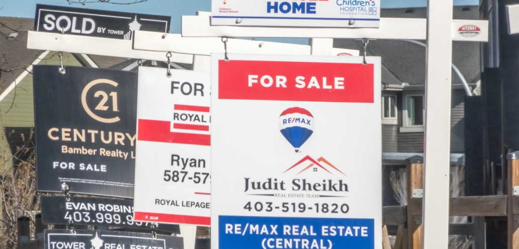 A row of real estate signs, including "For Sale" and "Sold" notices, from various companies such as RE/MAX, Royal LePage, and Century 21, are displayed in front of multiple houses.