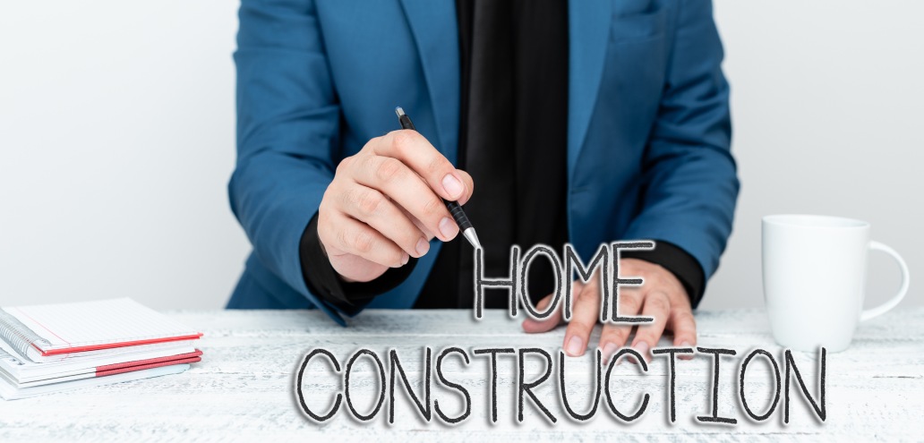 Person in a blue blazer holding a pen sits at a white table with a notebook, coffee cup, and the words "Home Construction" written in front.