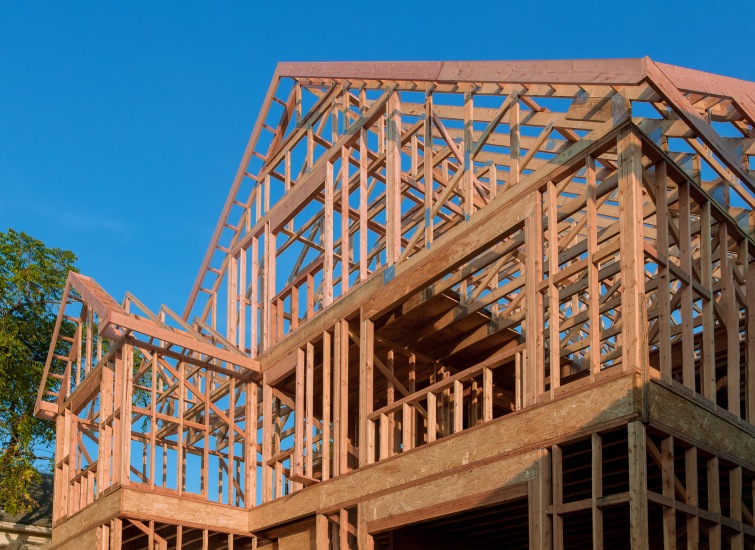 A partially constructed wooden house frame under a clear blue sky.